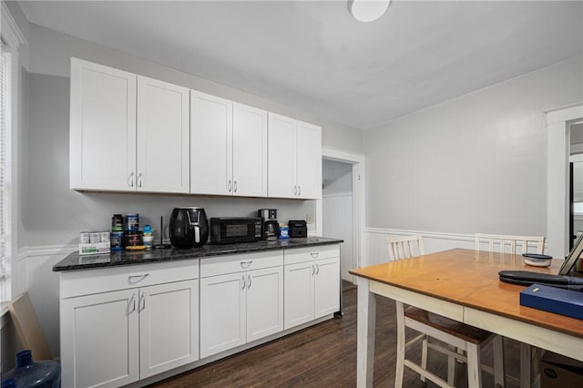 kitchen featuring a wainscoted wall, dark wood-style flooring, white cabinets, and dark stone counters