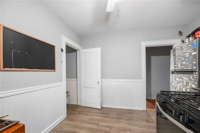 kitchen featuring wood finished floors, wainscoting, range with gas cooktop, and a ceiling fan