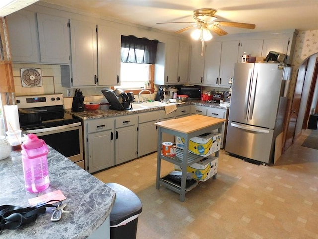 kitchen with stainless steel appliances, light flooring, a ceiling fan, a sink, and backsplash