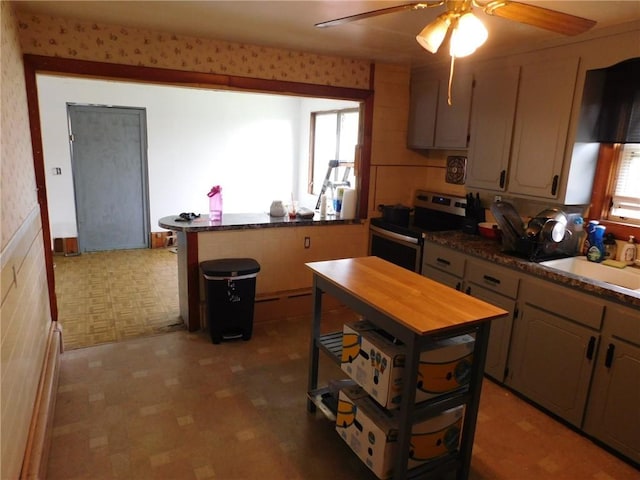 kitchen with stainless steel range with electric stovetop, a sink, a ceiling fan, a peninsula, and dark countertops