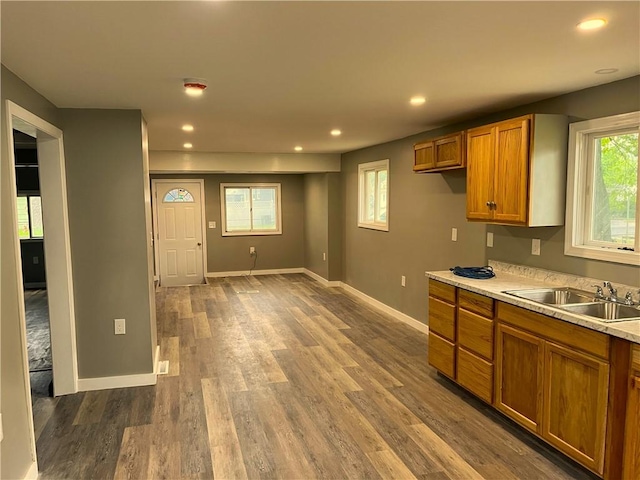 kitchen with brown cabinetry, dark wood-style floors, a sink, baseboards, and recessed lighting