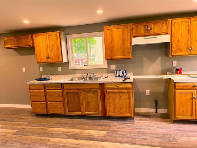 kitchen with under cabinet range hood, a sink, baseboards, light countertops, and recessed lighting