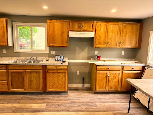 kitchen with a sink, under cabinet range hood, light countertops, brown cabinets, and recessed lighting