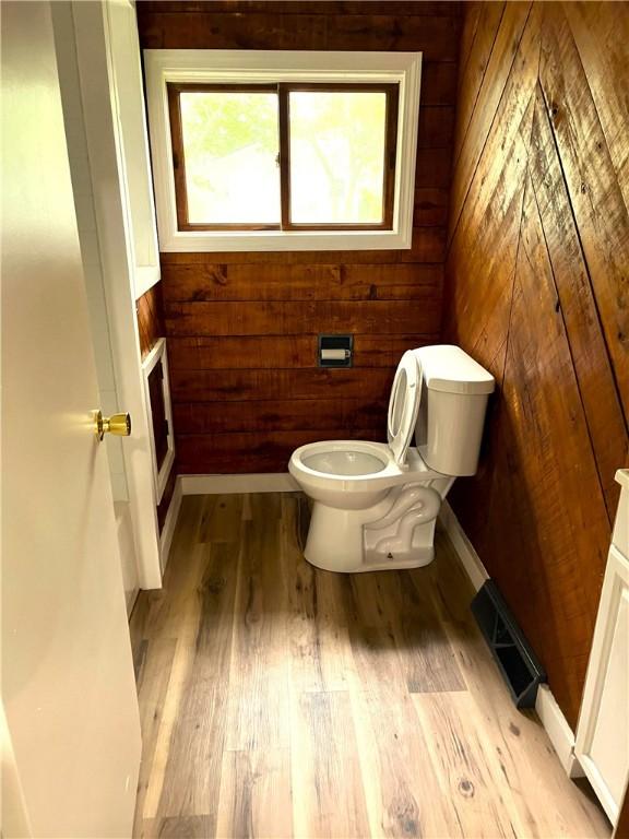 bathroom featuring wood walls, toilet, and wood finished floors