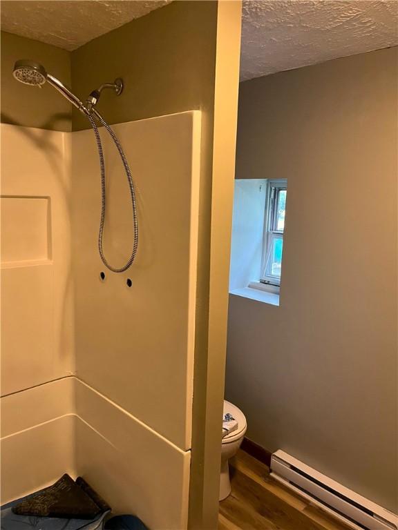 bathroom with baseboard heating, wood finished floors, a textured ceiling, toilet, and a shower