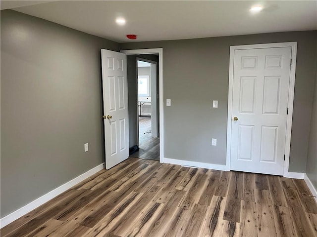 unfurnished bedroom featuring baseboards, wood finished floors, and recessed lighting