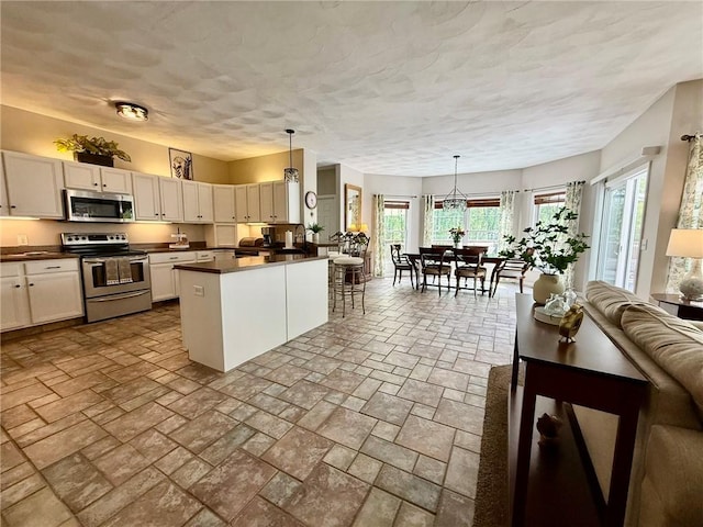 36 Jasmine Cir, North Kingstown, RI 02874 - kitchen featuring stainless steel appliances, dark countertops, a peninsula, open floor plan, and stone tile flooring