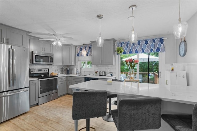 52 Eddy St, North Providence, RI 02911 - kitchen with stainless steel appliances, gray cabinets, tasteful backsplash, light wood-style floors, and hanging light fixtures