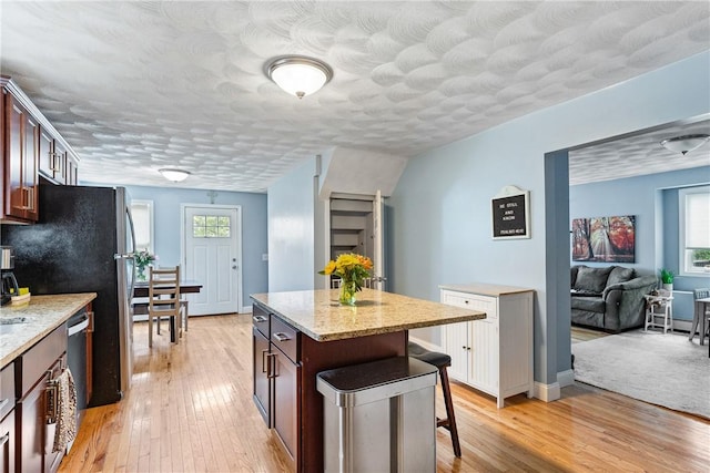 27 Aberdeen St, West Warwick, RI 02893 - kitchen with a breakfast bar area, light wood-style floors, light stone counters, a kitchen island, and a textured ceiling