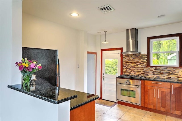 77 Glen Ave, Cranston, RI 02905 - kitchen with appliances with stainless steel finishes, wall chimney range hood, brown cabinets, backsplash, and dark stone counters