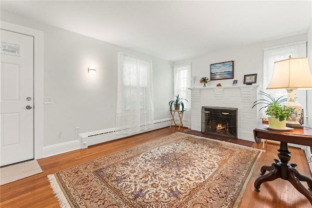12 Arlington St, Westerly, RI 02891 - living area featuring a baseboard heating unit, a brick fireplace, wood finished floors, and baseboards
