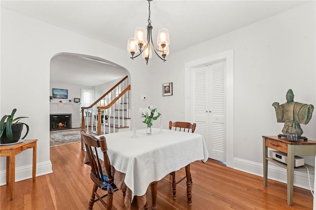 12 Arlington St, Westerly, RI 02891 - dining space featuring arched walkways, baseboards, light wood-style floors, a warm lit fireplace, and a chandelier