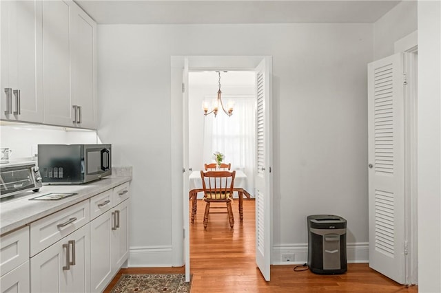 12 Arlington St, Westerly, RI 02891 - kitchen with stainless steel microwave, light wood-type flooring, a chandelier, light countertops, and white cabinets