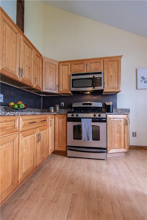 417 Privilege St, Woonsocket, RI 02895 - kitchen featuring appliances with stainless steel finishes, light wood-type flooring, lofted ceiling, backsplash, and dark stone counters