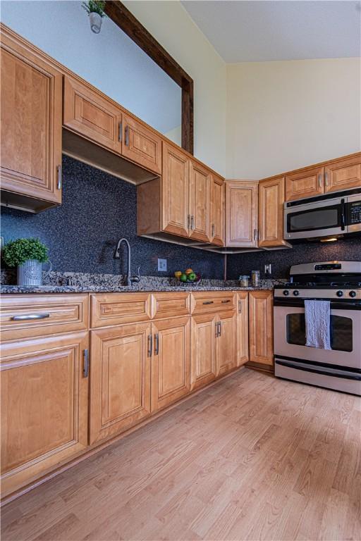 417 Privilege St, Woonsocket, RI 02895 - kitchen with appliances with stainless steel finishes, dark stone counters, a sink, light wood-style flooring, and decorative backsplash