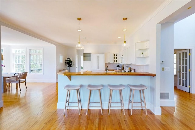 38 Westwind Dr, Jamestown, RI 02835 - kitchen with white cabinets, baseboards, light wood-style floors, a peninsula, and crown molding