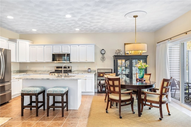 83 Preservation Way S, Kingstown, RI 02879 - kitchen with stainless steel appliances, white cabinets, a center island with sink, light tile patterned floors, and light stone counters