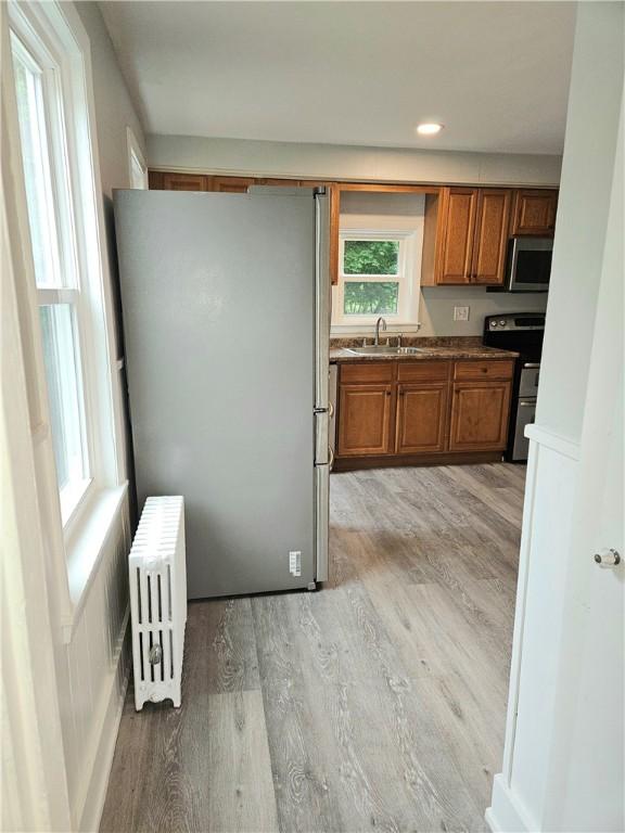 29 Arthur St, Warwick, RI 02888 - kitchen with radiator, stainless steel appliances, a sink, brown cabinetry, and light wood-style flooring