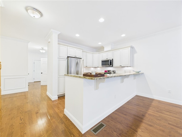 147 Southwinds Dr, South Kingstown, RI 02879 - kitchen featuring stainless steel appliances, a peninsula, crown molding, light wood-style flooring, and stone counters