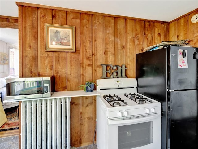 219 Nanaquaket Rd, Tiverton, RI 02878 - kitchen featuring white gas range, freestanding refrigerator, radiator heating unit, wood walls, and brown cabinets