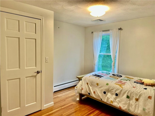 261 John Potter Rd, West Greenwich, RI 02817 - bedroom with baseboard heating, light wood-type flooring, and a textured ceiling