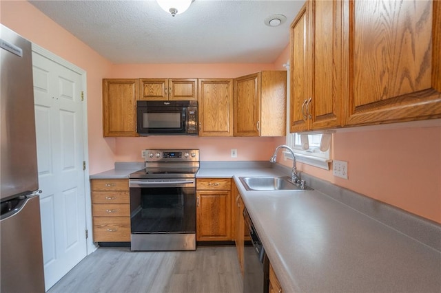 26 Noel Ct, South Kingstown, RI 02879 - kitchen featuring stainless steel appliances, a sink, light wood-style flooring, brown cabinets, and a textured ceiling