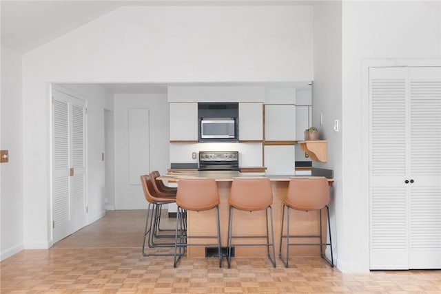 3 Ernest St, Newport, RI 02840 - kitchen featuring appliances with stainless steel finishes, a kitchen bar, white cabinets, baseboards, and a peninsula