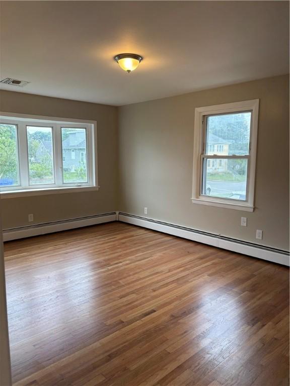 173 Martin St, East Providence, RI 02914 - empty room featuring plenty of natural light, wood finished floors, and a baseboard heating unit