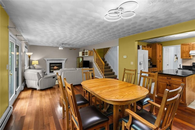 53 Morgan Ct, North Kingstown, RI 02852 - dining area with baseboard heating, hardwood / wood-style flooring, stairway, a warm lit fireplace, and ceiling fan