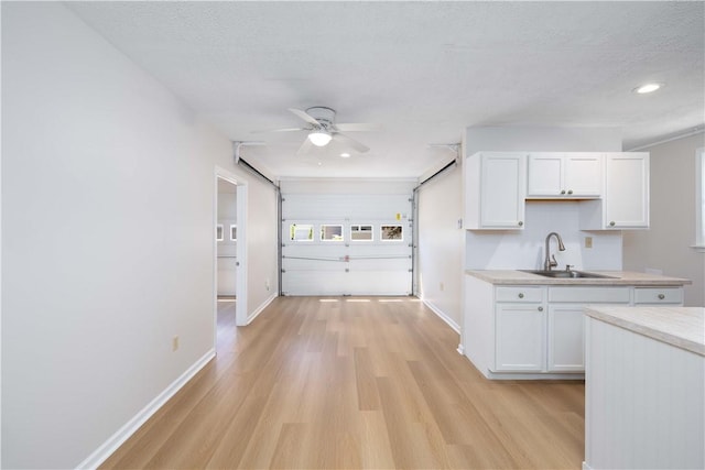 130 Hunts Ave, Pawtucket, RI 02861 - kitchen featuring a sink, light wood finished floors, white cabinets, baseboards, and a textured ceiling