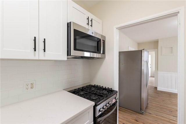 9 Woodbine St, Providence, RI 02906 - kitchen with stainless steel appliances, light wood-style floors, white cabinetry, decorative backsplash, and light stone counters