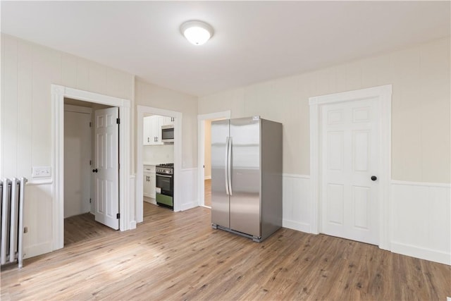 9 Woodbine St, Providence, RI 02906 - unfurnished bedroom with freestanding refrigerator, light wood finished floors, radiator heating unit, and a decorative wall