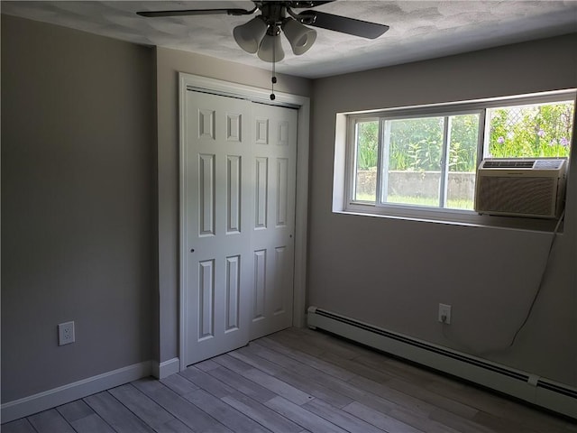 56 River St Unit 23, West Warwick, RI 02893 - unfurnished bedroom with a baseboard radiator, wood finished floors, a closet, ceiling fan, and baseboards