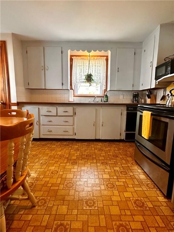 100 Benedict St, Pawtucket, RI 02861 - kitchen featuring stainless steel range with electric cooktop, black microwave, decorative backsplash, and brick patterned flooring