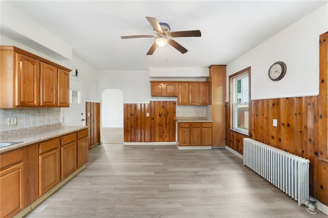 1875 Smith St, North Providence, RI 02911 - kitchen with radiator heating unit, a ceiling fan, light wood-style floors, brown cabinetry, and a wainscoted wall