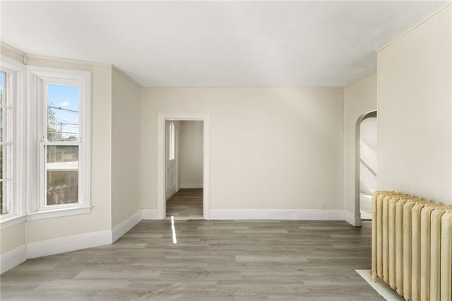1875 Smith St, North Providence, RI 02911 - empty room with radiator heating unit, baseboards, light wood finished floors, and arched walkways