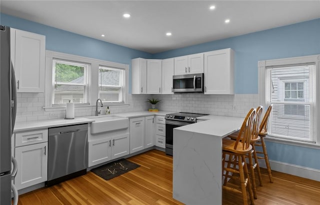 36 Ruth Ave, East Providence, RI 02916 - kitchen with appliances with stainless steel finishes, a sink, a kitchen bar, white cabinets, and light wood-style floors