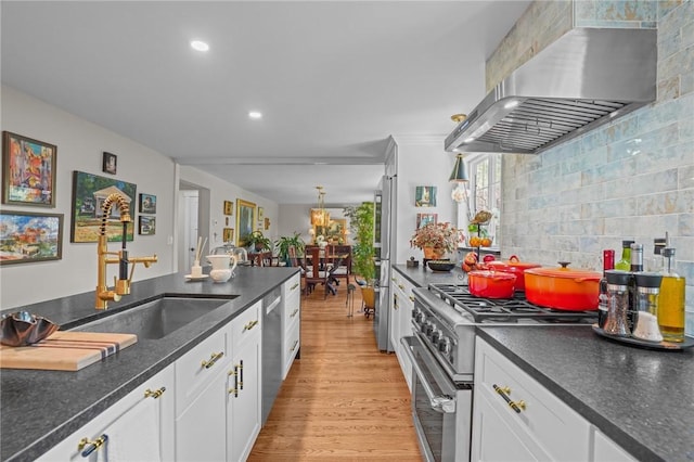 25 King Philip Rd, Pawtucket, RI 02861 - kitchen featuring wall chimney range hood, stainless steel appliances, a sink, white cabinets, and light wood-style flooring