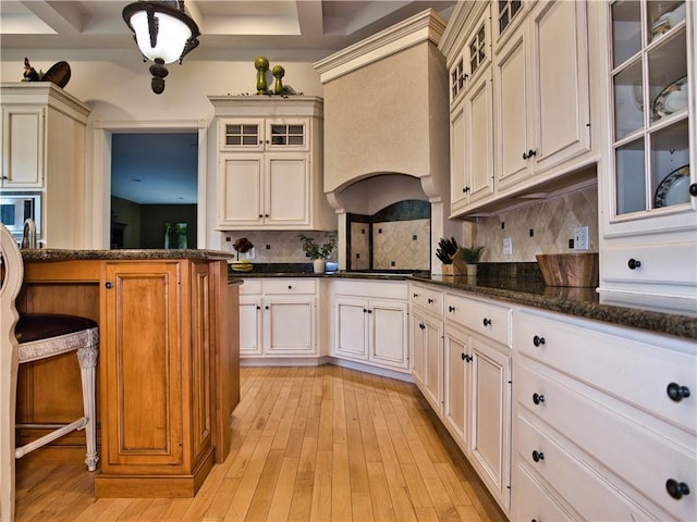 51 W Ridge Dr, Tiverton, RI 02878 - kitchen featuring decorative backsplash, premium range hood, light wood-style flooring, dark stone countertops, and glass insert cabinets