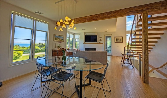 1448 Mohegan Trl, Block Island, RI 02807 - dining room with light wood-style flooring, stairway, a fireplace, beam ceiling, and a chandelier