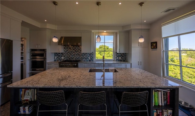 1448 Mohegan Trl, Block Island, RI 02807 - kitchen with a sink, stainless steel double oven, exhaust hood, backsplash, and a center island with sink