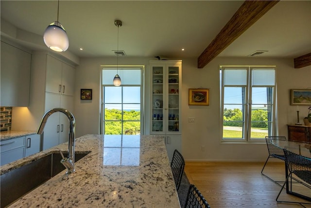 1448 Mohegan Trl, Block Island, RI 02807 - kitchen with a sink, light wood-style flooring, beam ceiling, white cabinetry, and light stone countertops