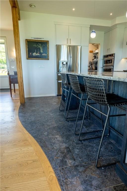 1448 Mohegan Trl, Block Island, RI 02807 - kitchen featuring appliances with stainless steel finishes, a breakfast bar, white cabinets, light stone countertops, and decorative light fixtures