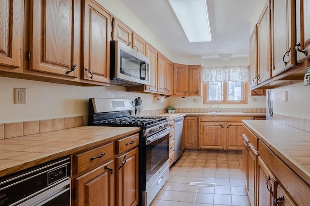 254 Jenckes St, Woonsocket, RI 02895 - kitchen featuring appliances with stainless steel finishes, tile countertops, a sink, light tile patterned floors, and brown cabinets