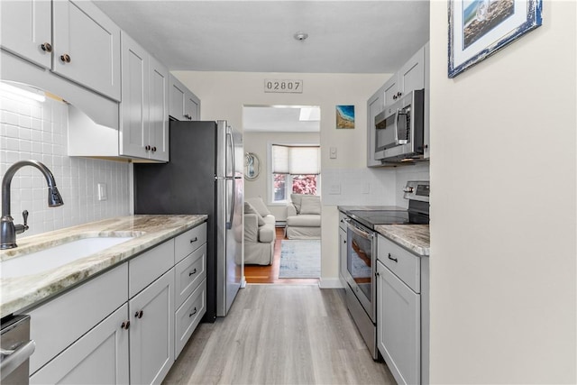 30 Brown St Unit 2, Narragansett, RI 02882 - kitchen featuring appliances with stainless steel finishes, a sink, light wood-style flooring, decorative backsplash, and light stone counters