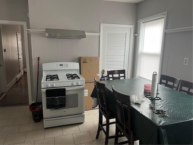 1097 Pontiac Ave, Cranston, RI 02910 - kitchen featuring white gas range, wall chimney range hood, a baseboard radiator, wainscoting, and light tile patterned flooring