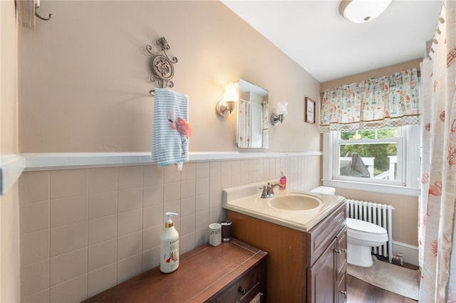 62 Andrews Ave, West Warwick, RI 02893 - bathroom with radiator heating unit, toilet, vanity, a wainscoted wall, and tile walls