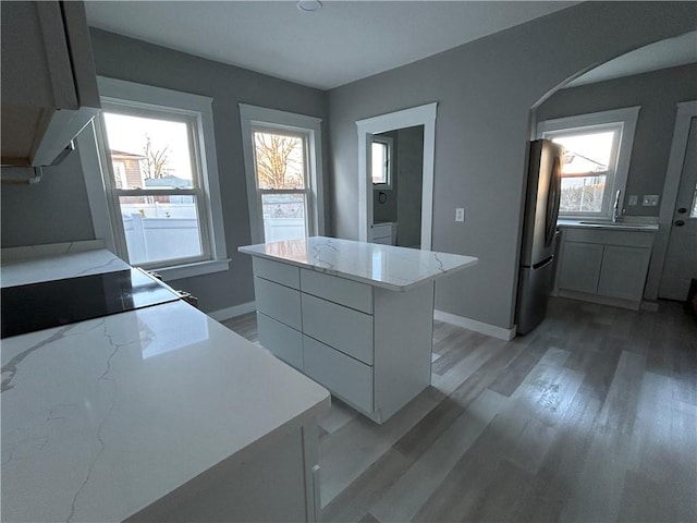 26 Mayflower St, East Providence, RI 02914 - kitchen featuring freestanding refrigerator, arched walkways, white cabinets, light wood-style floors, and baseboards