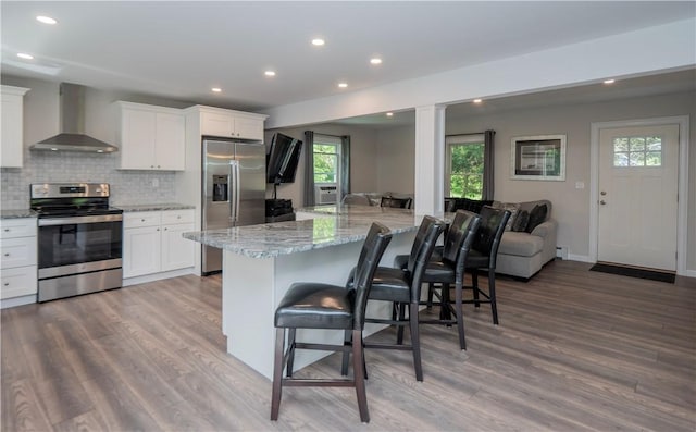 126 Hilton St, Tiverton, RI 02878 - kitchen with appliances with stainless steel finishes, wall chimney range hood, a breakfast bar area, wood finished floors, and white cabinets