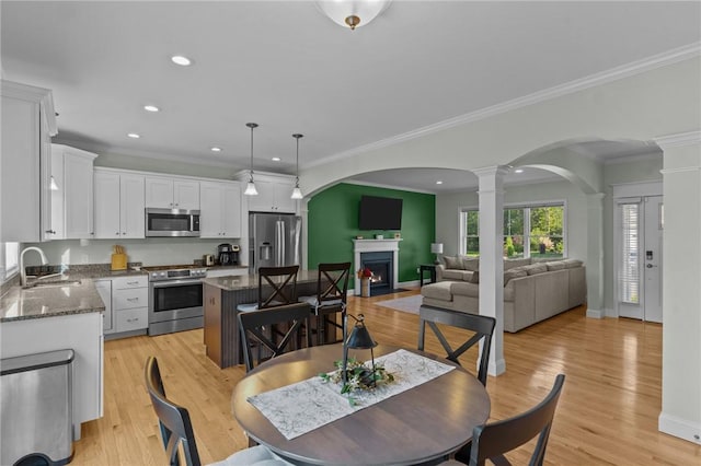 25 Ironwood Dr, Coventry, RI 02816 - dining area featuring ornate columns, arched walkways, a warm lit fireplace, ornamental molding, and light wood finished floors